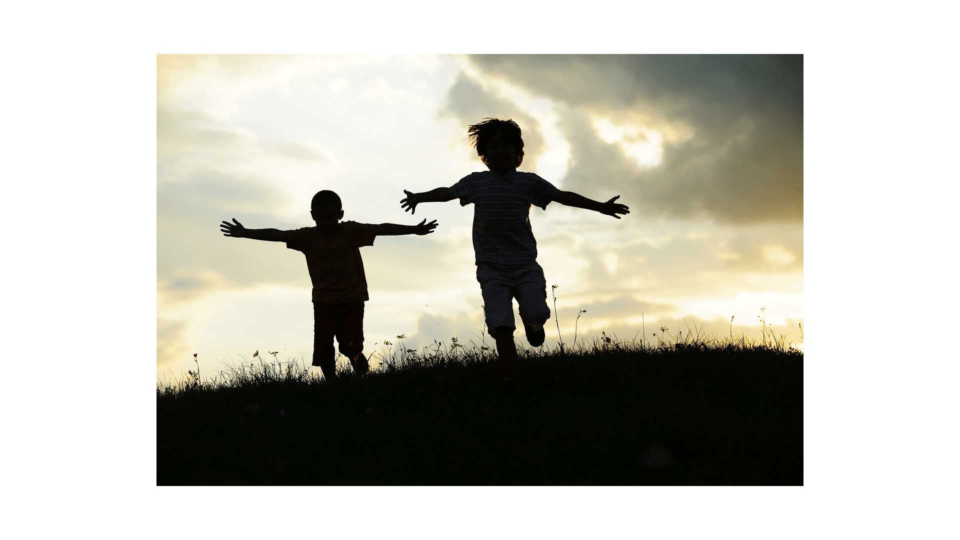 Slihouette of two children leaping on a hill in the sunlight outdoors